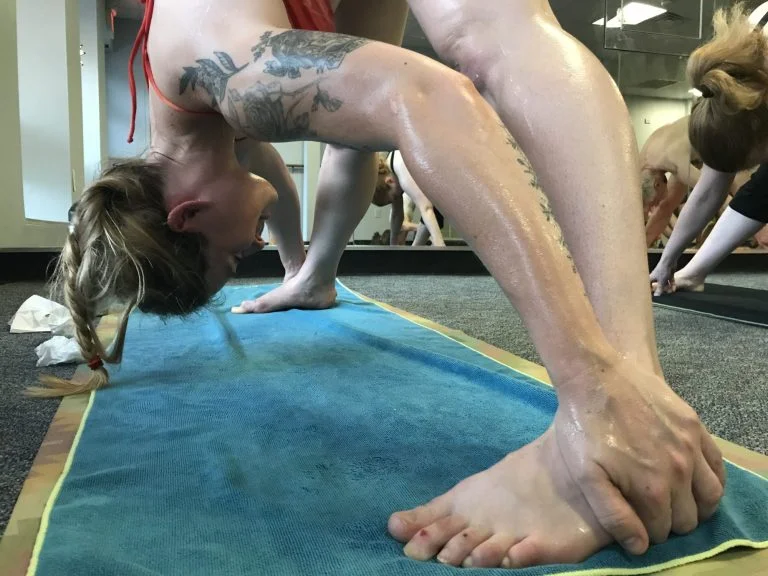 Hot yoga session featuring a woman in a back-bending bow pose on a mat during a fitness class